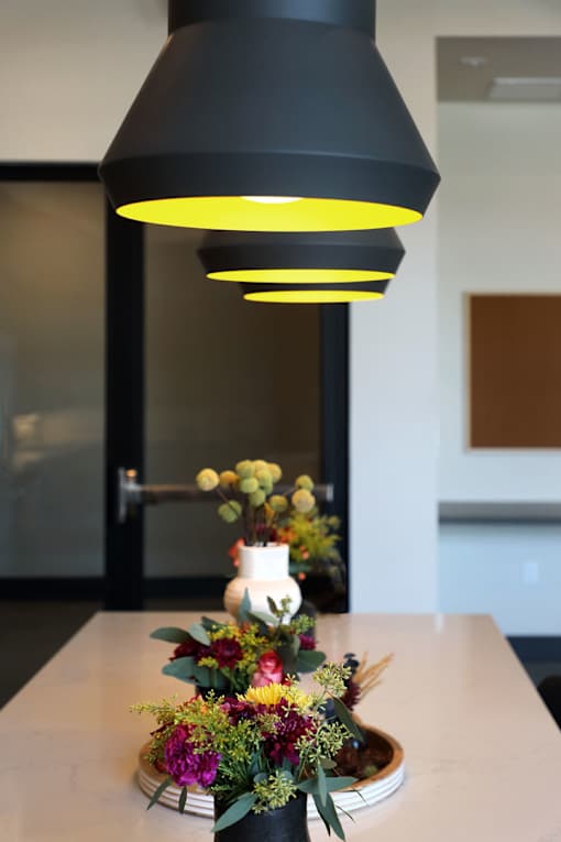 A black lamp with a yellow glow hangs over a table with a floral arrangement.