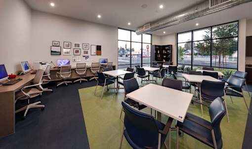 A room with tables and chairs and a computer on a desk.