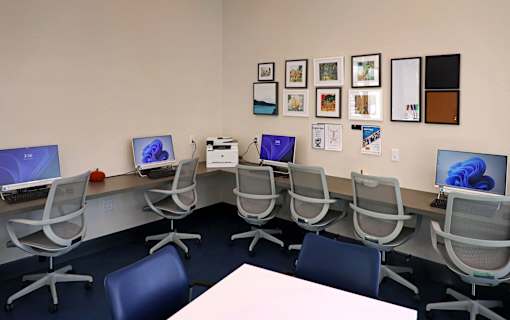 A room with a white table and chairs with a computer on each chair.