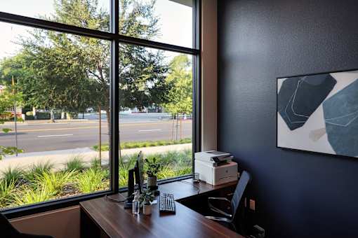 A room with a desk, a computer, a printer, and a painting on the wall.