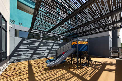 A playground slide is located on a wooden deck under a metal roof.