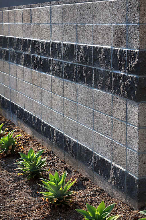 A wall made of grey blocks with plants in front.