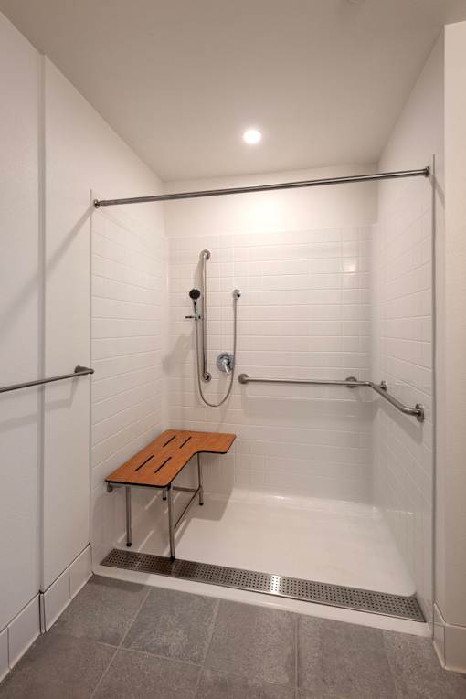 A white tiled shower with a bench and a metal drain.