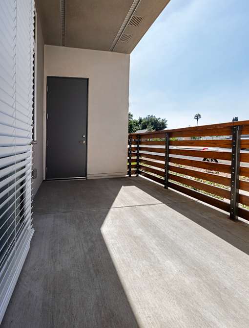 A black door is at the end of a hallway with a wooden fence on the right.