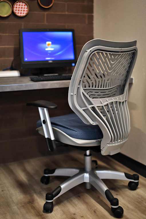A white chair with a blue cushion is in front of a computer monitor.