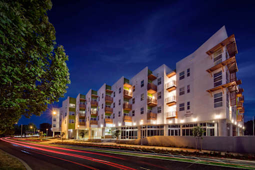 A modern apartment building is lit up at night with cars passing by on the street.