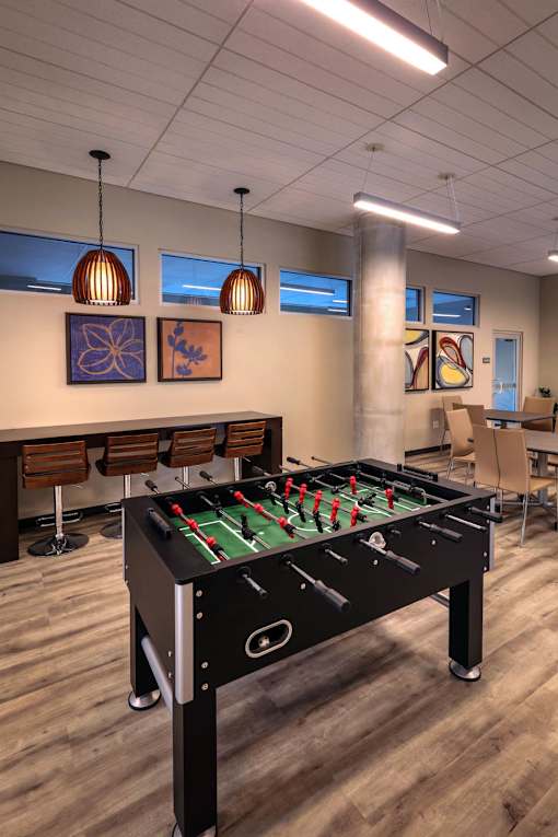 A foosball table is in the middle of a room with chairs and artwork on the wall.
