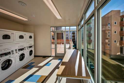 A laundry room with a bench and a row of washing machines.