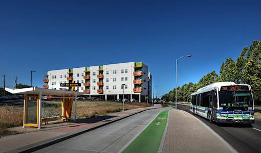 A bus is driving on a road with a bus stop on the left.