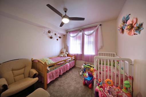 A room with a ceiling fan and two beds with toys on the floor.