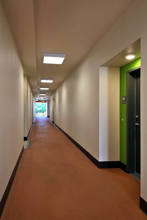 A long hallway with green doors and brown floors.