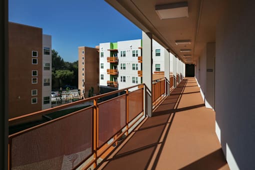 A long corridor with a metal railing on the left side and buildings on the right.