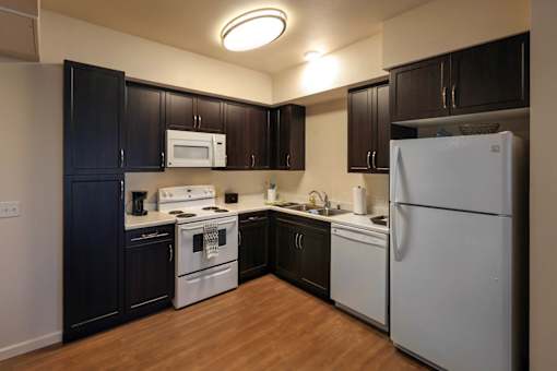 A kitchen with a white refrigerator, black cabinets, and a white stove top oven.
