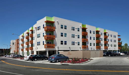 A white building with orange balconies and a parking lot in front.