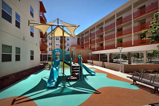 A playground with a blue slide and a yellow umbrella.