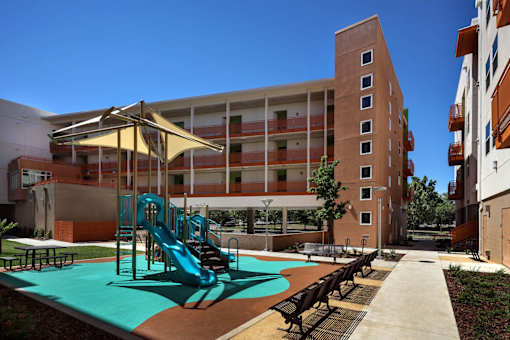 A playground with a slide and a bench in front of a building.
