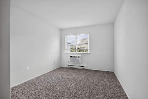 A room with a carpet floor and a window with blinds.