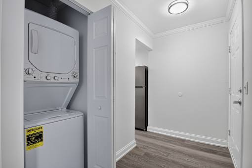 A small white fridge with a yellow sticker on it is in a room with a black fridge in the background.