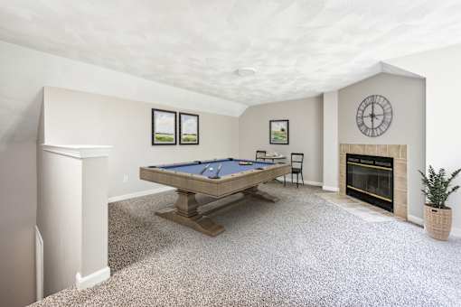 A loft space with pool table in a room with a fireplace and a clock on the wall with carpet floor at Birchwood Hills Townhomes in Shirley, MA.