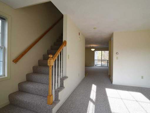 A non-renovate home at Birchwood Hills Townhomes showing the staircase and hallway connecting the living room and kitchen.