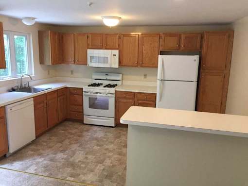 A kitchen with white appliances and wooden cabinets at Birchwood Hills in Shirely, MA.