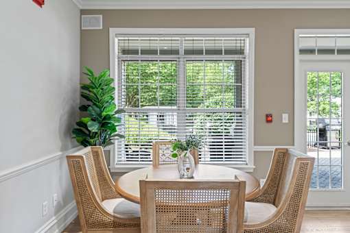 A table with chairs and a vase of flowers in front of a window.