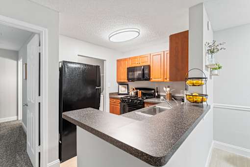 A kitchen with a black refrigerator and wooden cabinets.