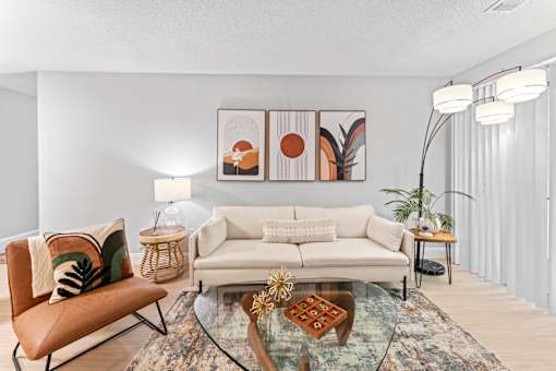 A living room with a white couch, a glass coffee table, and a chair.
