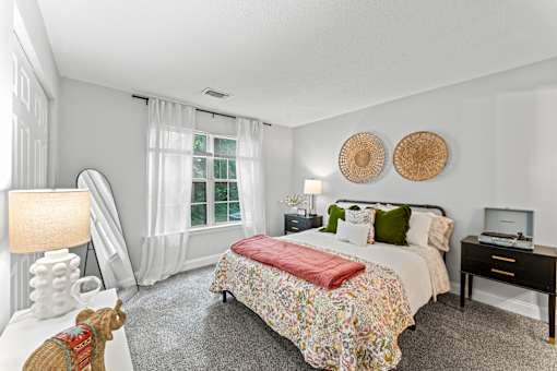 A bedroom with a large bed and a window with white curtains.