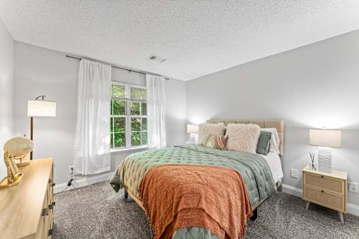 A bedroom with a bed, nightstand, and window.