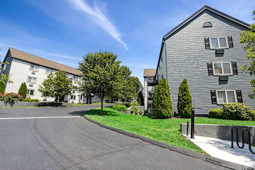 A sunny day at a residential area with two buildings and a tree.