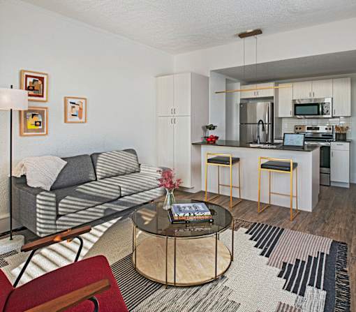 A modern living room with a grey couch, a coffee table, and a kitchen in the background.