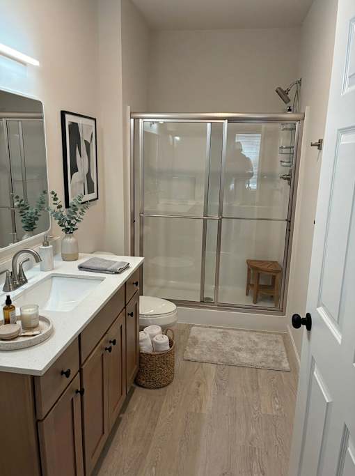A bathroom with a sink, mirror, toilet, and a glass shower door.