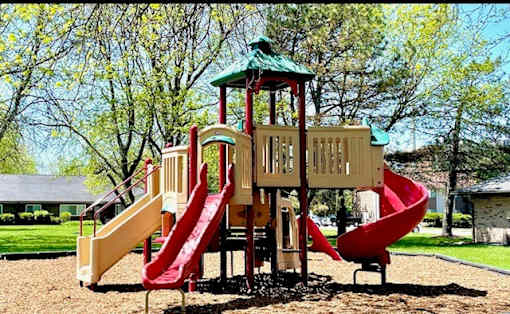 A playground with a red and yellow slide and a green roof.