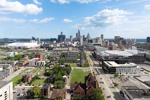 A cityscape with a mix of modern and older buildings, a large open grassy area, and a clear sky.