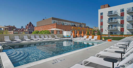A pool with chairs around it and a building in the background.