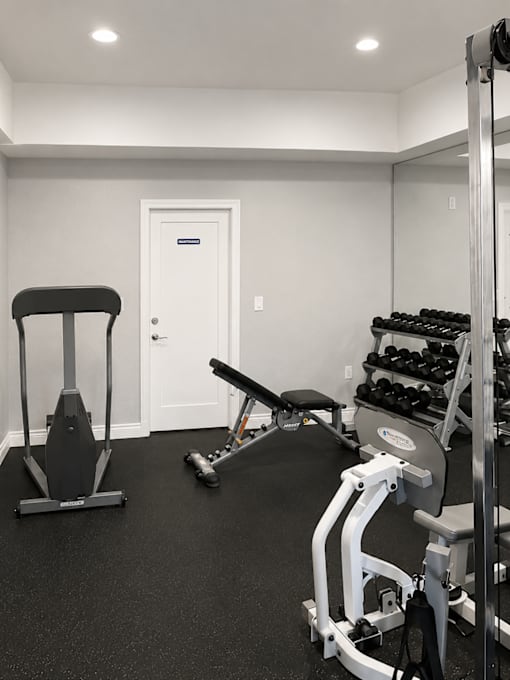A black and white photo of a home gym with a squat rack, bench, and dumbbells.