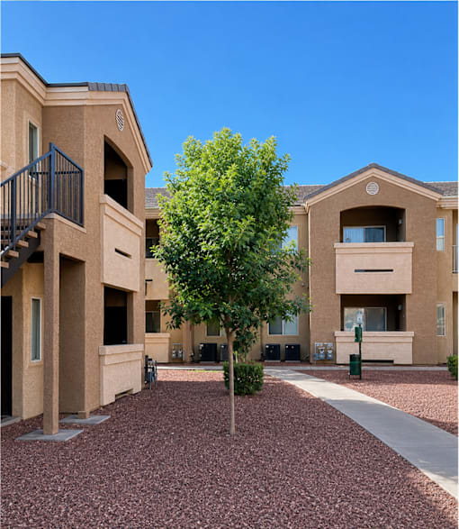 A tree in front of a building with a red brick ground.