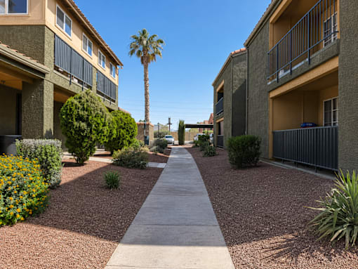 A pathway leads through a landscaped courtyard between two apartment buildings.