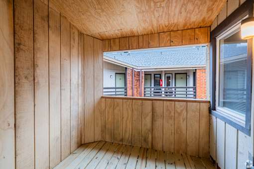 A wooden room with a window overlooking a red brick building.