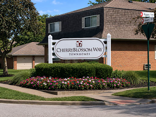 A sign for Cherryblossom Way townhomes stands in front of a brick building.