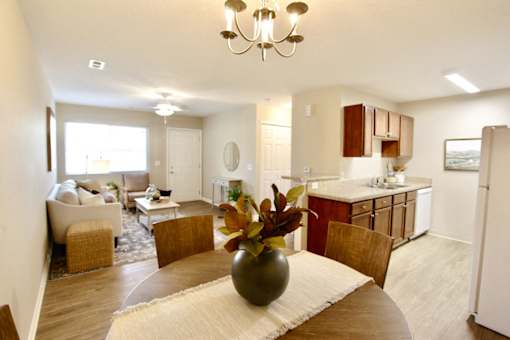 A well-lit, spacious kitchen and living room with a chandelier and a vase of flowers on the coffee table.