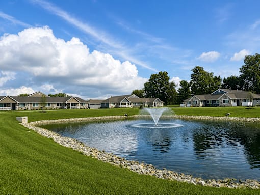 A fountain in the middle of a pond surrounded by grass.
