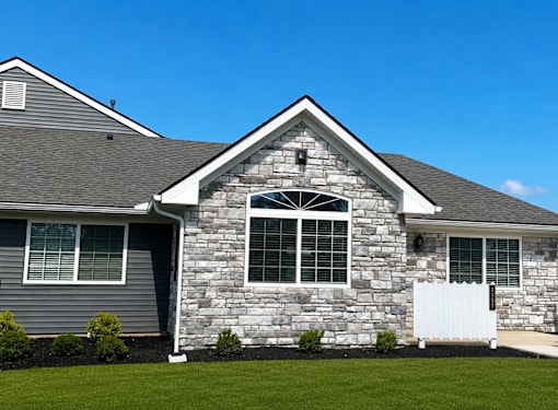 A house with a grey siding and a stone facade with a white fence in front.