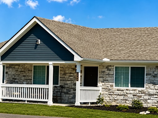 An apartment building with blue siding and rock with a porch that has white railings.