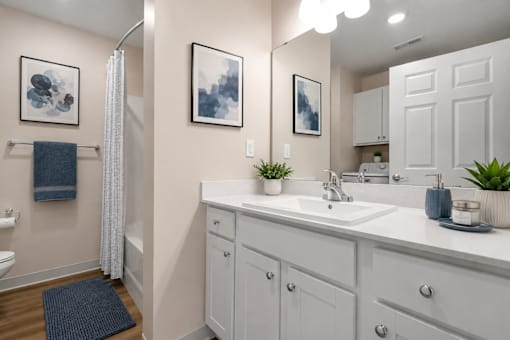 A bathroom with toilet, shower, white cabinets and countertop.