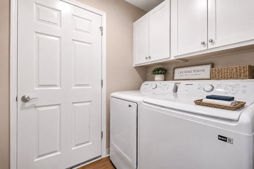 A laundry are with a washer and dryer and white cabinets.
