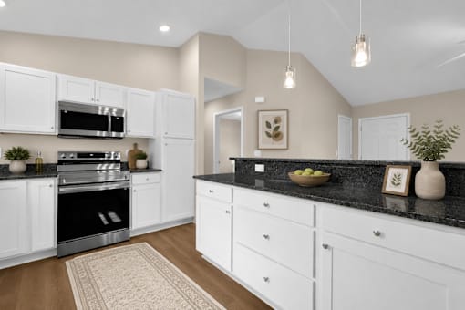A kitchen with white cabinets, black countertop, wood plank floor and stainless steel appliances.