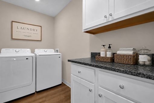A laundry area with a washer and dryer and white cabinets with a black counterop.