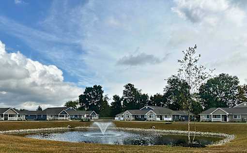 a fountain in the middle of a pond in front of houses